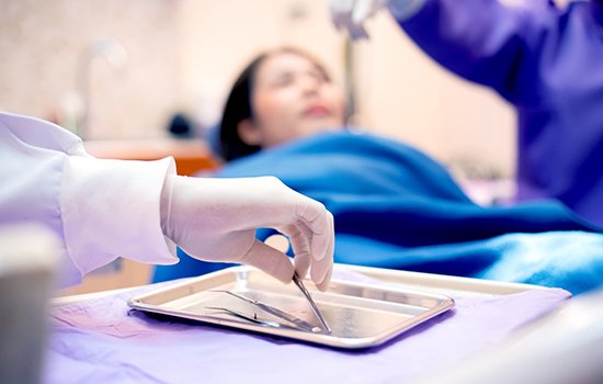 A gloved hand holding a dental tool while a patient receives care in the background