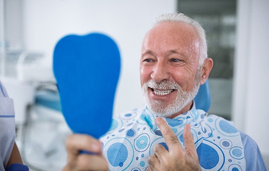 Senior man smiling at reflection in handheld mirror