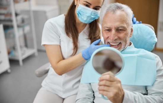 Senior dental patient looking at his smile in mirror