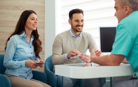 Two patients and dental team member discussing the cost of dental implants