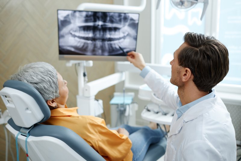 A dentist pointing to a patient’s dental X-rays